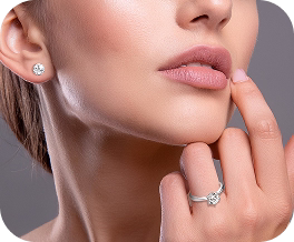 Close do rosto feminino destacando brinco pequeno de diamante e anel de noivado prateado.
