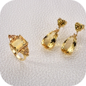Brincos dourados com pedras em formato de gota âmbar, sobre fundo claro.