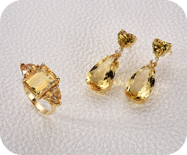 Brincos dourados com pedras em formato de gota âmbar, sobre fundo claro.